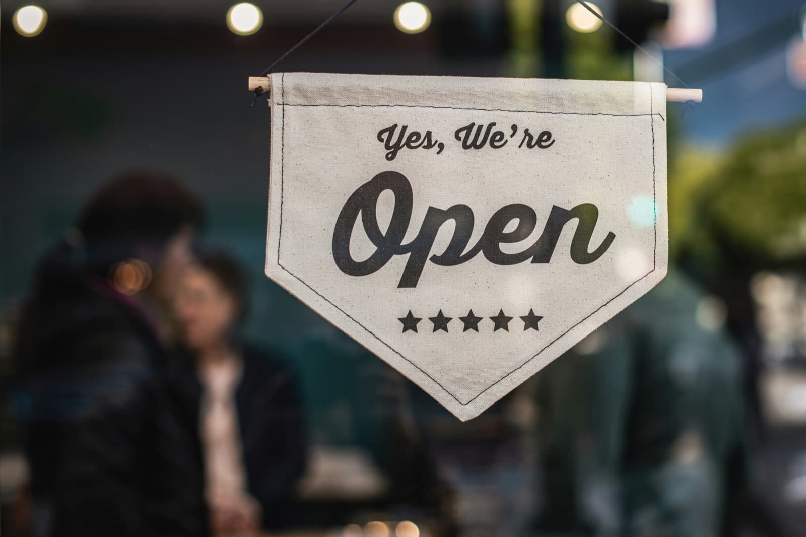 A hanging fabric sign reading “Yes, We're Open” in a shop window